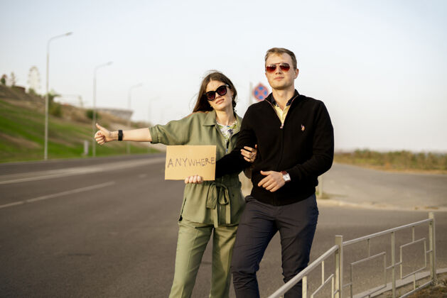 两个一对年轻夫妇一家搭便车在高速公路上等车 带着爱自由旅行爱情情侣度假