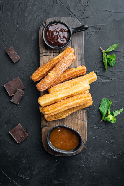 面包房典型的西班牙小吃churros 油炸面团 通常配巧克力焦糖辣酱 黑色背景 俯视平面图热烘焙棒