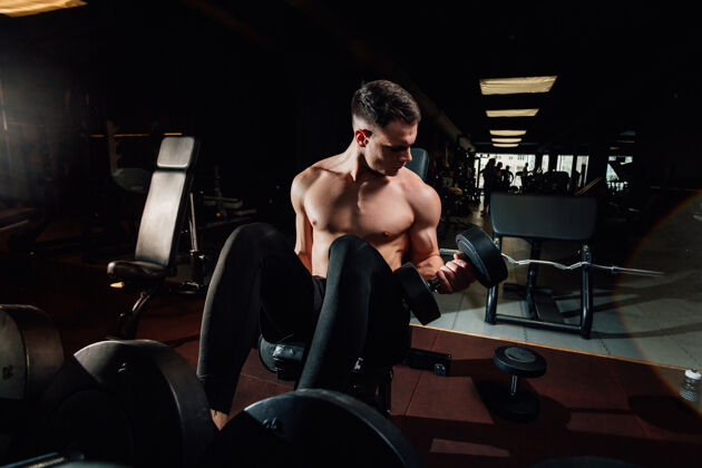 哑铃帅气的肌肉男 站在黑暗的现代体育馆里 用沉重的哑铃锻炼身体帅气运动员肌肉
