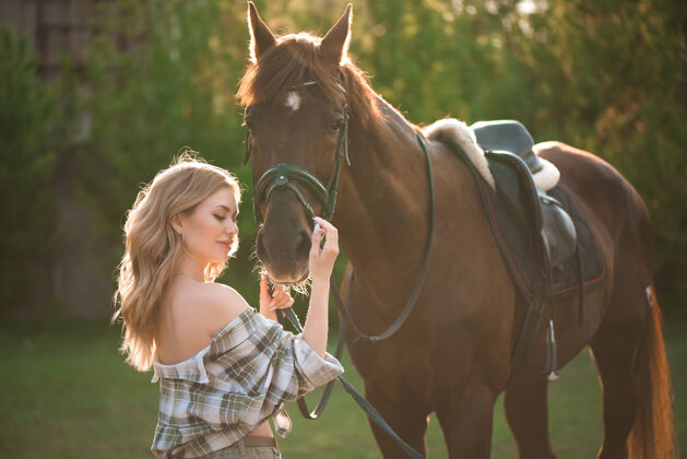 骑手在马场里穿着衬衫和黑马在一起的女孩的画像青少年金发马