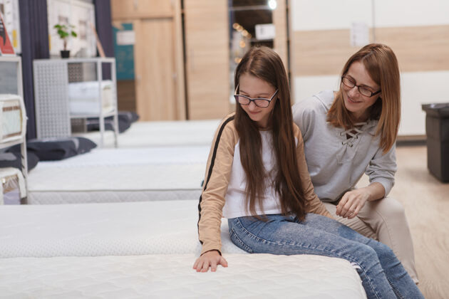 青少年十几岁的女孩和她的母亲在家具店选择骨科床垫消费主义商店年轻