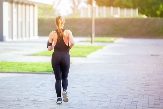 早晨穿着运动服的女人在城里沿着房子跑运动跑步运动员