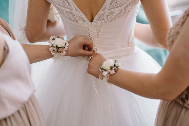 白天伴娘在婚礼前帮新娘系上白色婚纱的花边细节背部紧身胸衣