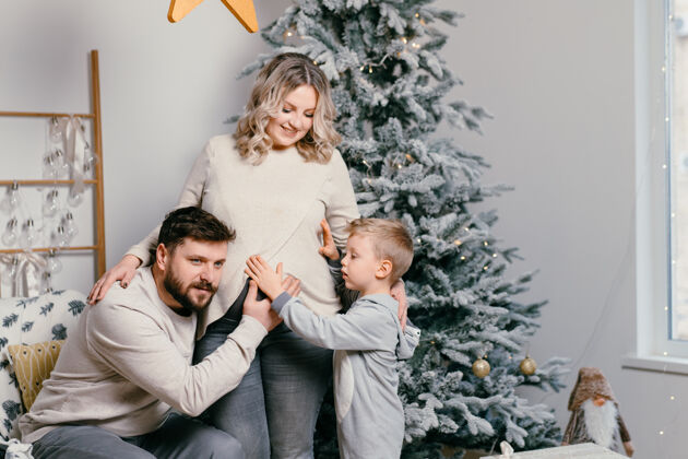 快乐圣诞家庭幸福写真爸爸 怀孕的妈妈和小儿子坐在家里的扶手椅旁圣诞树拥抱微笑欧洲年轻人家庭节日的早晨童年节日小