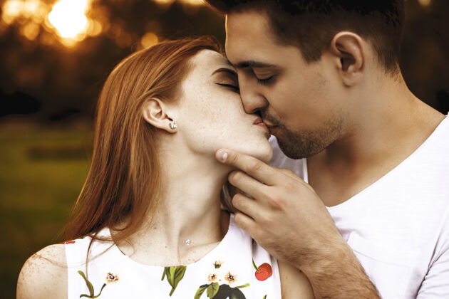 关系一对迷人的年轻情侣在夕阳下闭着眼睛接吻的侧视图 而男人正抚摸着他女朋友的脸爱特写女性