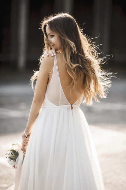 年轻一位美丽的年轻新娘的后视图 她留着一头长发 举着一个水桶 在日出的映衬下微笑着看着身后欢呼手优雅
