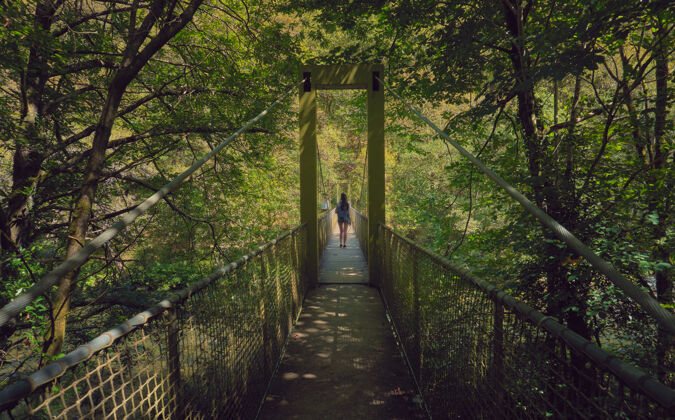 旅行阳光明媚的夏天 年轻女子在森林里过吊桥白天森林的加利西亚圣地亚哥我们的路公园女人旅游