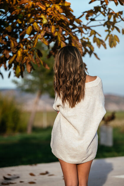柔软秋日院子里 一位穿着白毛衣的匿名女性站在枯叶的树枝旁漂亮女孩微笑