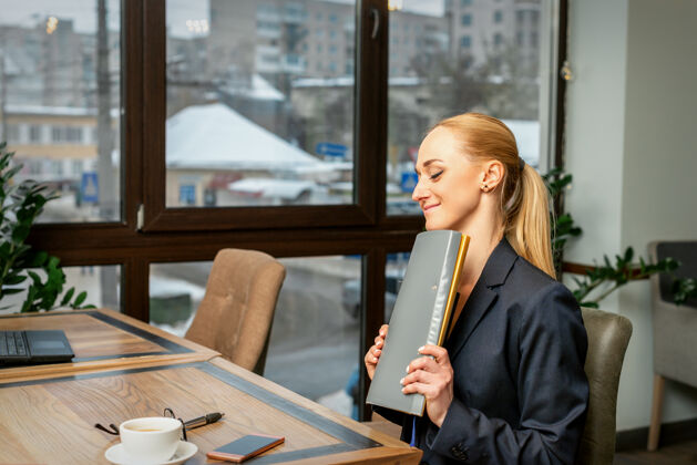 年轻在办公室或咖啡馆的桌子旁 年轻漂亮的白人女商人手里拿着一个文件夹 里面放着文件执行领导公司