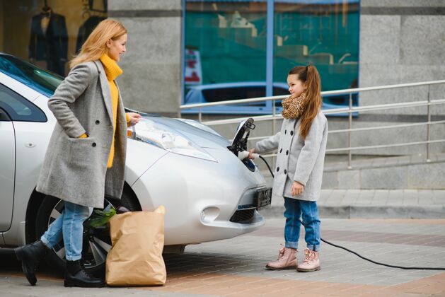 母亲一位时髦的母亲教她的女儿如何正确地给电动车充电驾驶员工业车站