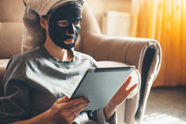 护理一位白人妇女在家戴着黑色面具 在地板上使用平板电脑的特写照片人面部身体