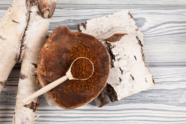 解毒木汤匙和干茶茶粉躺在一个天然的桦树蘑菇旁边的桦树树皮输液病原体蘑菇