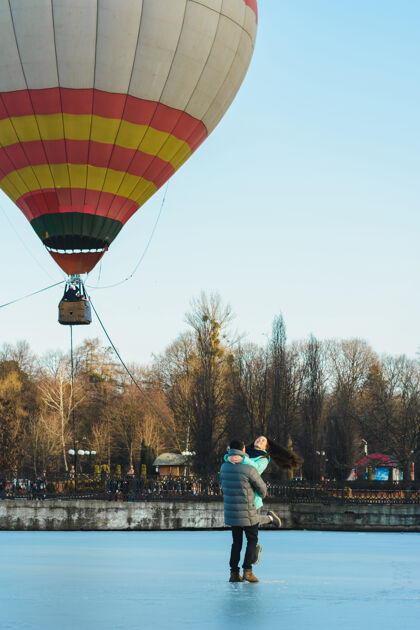 热新娘和新郎在冰冻的湖面和城市公园里飞行的气球的背景下年轻浪漫情侣