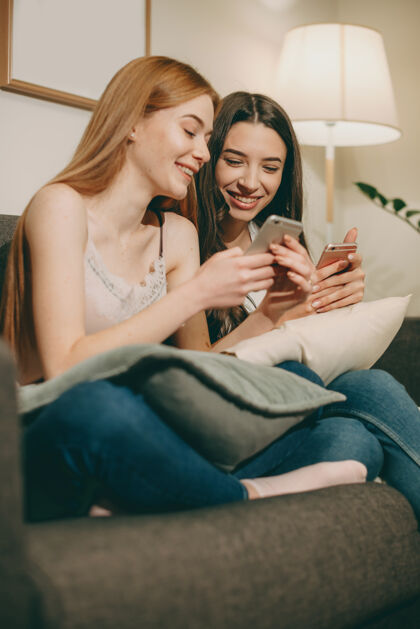 在线可爱的红发雀斑年轻女子坐在沙发上笑着向朋友展示智能手机屏幕上的东西社交肖像姐姐