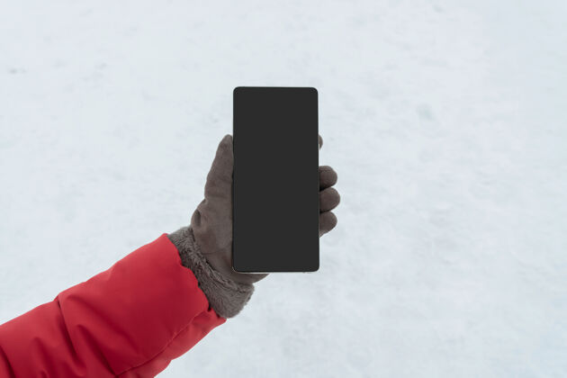 雪女性手在冬季手套举行智能手机与空白屏幕复制空间 显示空白屏幕