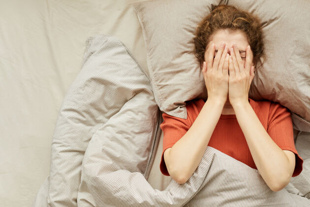 睡眠高角度的年轻女子用手捂着脸躺在床上疲倦舒适枕头