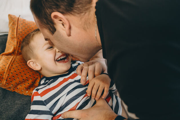 活动一个可爱的小儿子和他的父亲在他们家的床上玩耍的特写照片父亲室内玩