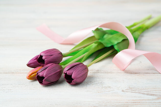 紫色一束带着丝带的花躺在一个浅色的木头上桌边查看 有空间复制花郁金香花束