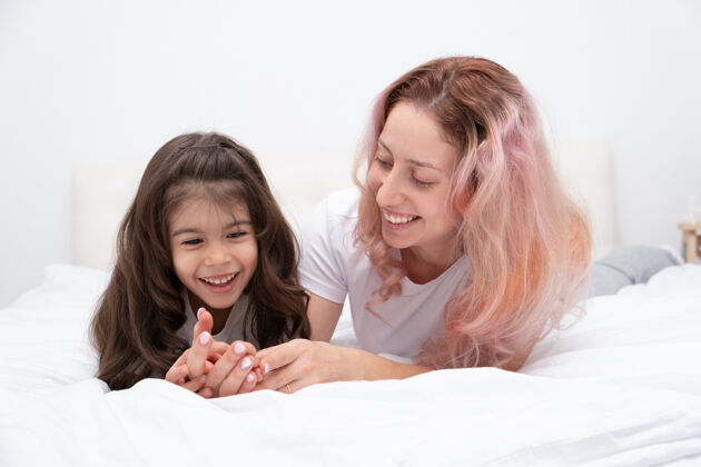 可爱的游戏妈妈带着活泼的小女儿在家里的床上玩耍 玩得开心 和孩子们一起活动无忧无虑的人两女在一起