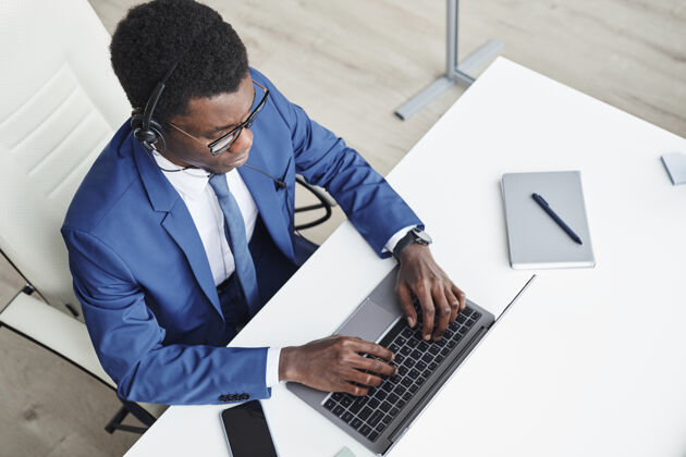 现代非洲商人戴着耳机在笔记本电脑上打字 在办公室的工作场所在线交流的高角度视图办公桌办公室坐姿