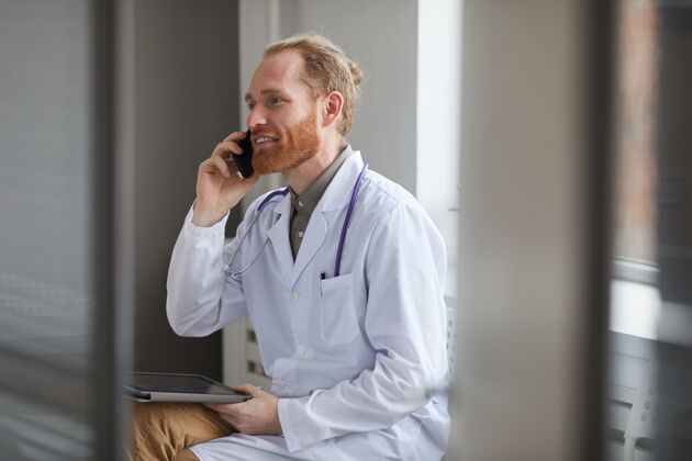 技术自信的白大褂医生坐在走廊边用手机聊天数字平板电脑听诊器室内
