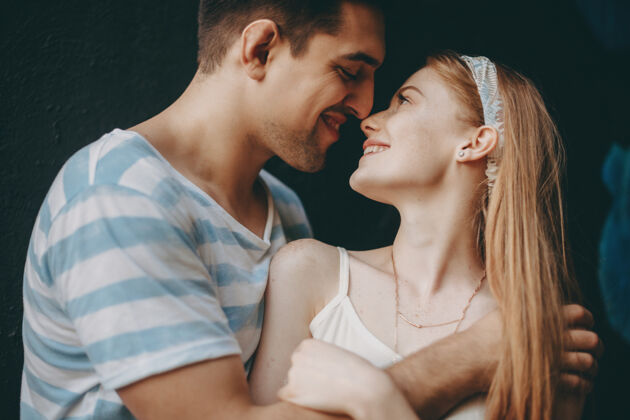约会一对美丽的年轻夫妇拥抱和微笑的侧视图 然后在室外的黑色墙壁上亲吻公园丈夫亲吻
