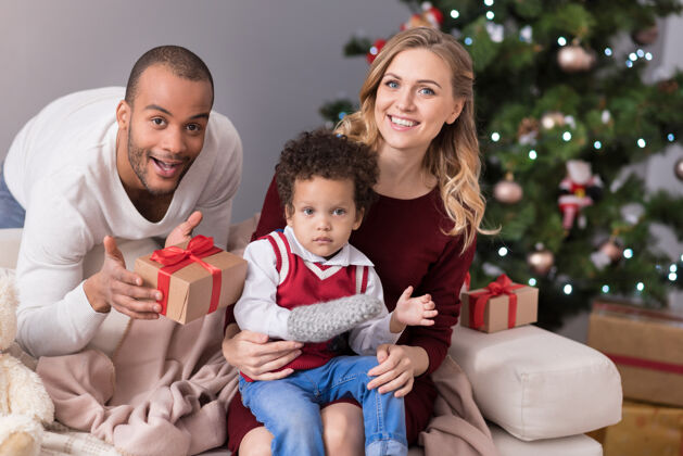 圣诞老人新年时间愉快积极的年轻家庭坐在圣诞树旁 看着你庆祝新年传统舒适父母