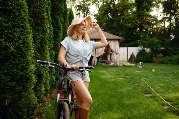 植物美丽的女园丁在公园里骑自行车花园女人户外自行车 园艺爱好 花店生活方式和休闲温室女孩铲子