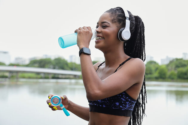 非洲人种快乐的年轻黑人健康女子在户外训练后饮用淡水运动员紧身裤耳机