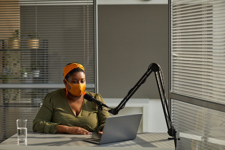 收音机戴着防护面具的年轻女子在直播过程中用笔记本电脑在线接受采访现代通信办公桌