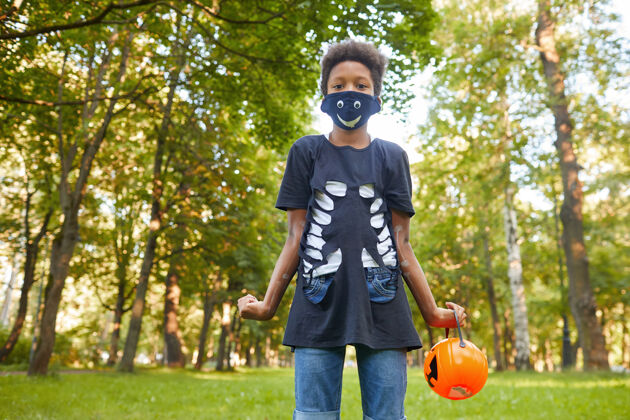 学龄前站在公园里穿着万圣节服装戴着面具的非洲男孩的画像休闲游戏服装超级英雄