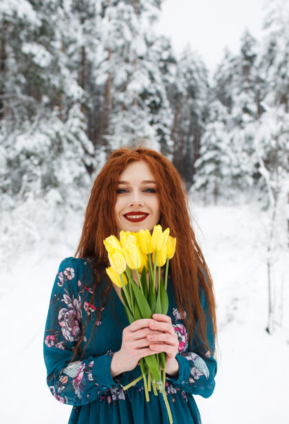 自然一个红头发的女孩拿着一束黄色郁金香在冬天的风景上红色雪户外