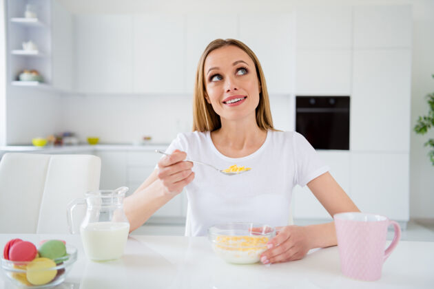 思考梦想家主妇拿着勺子吃早餐玉米片健康饮食看起来很梦幻想象自己下巴坐在桌子上白光厨房室内家庭主妇计划早餐