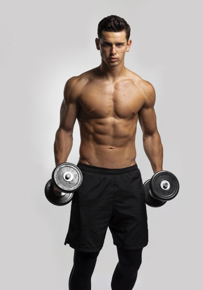 训练正面图片一个自信的年轻人赤膊上身训练哑铃 显示腹肌运动装强壮肌肉