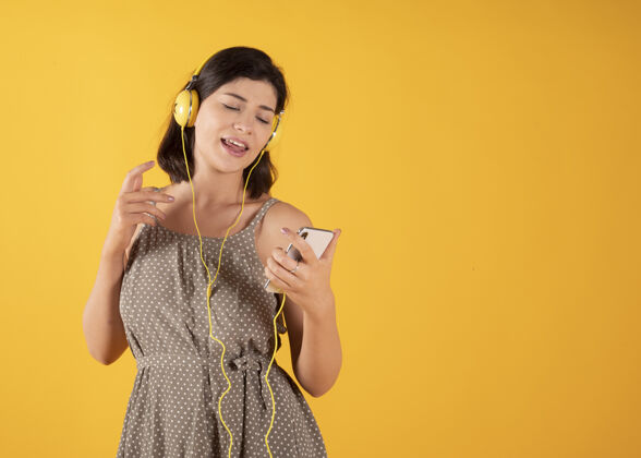 聆听戴着耳机和手机听音乐唱黄墙的女人休闲乐趣积极