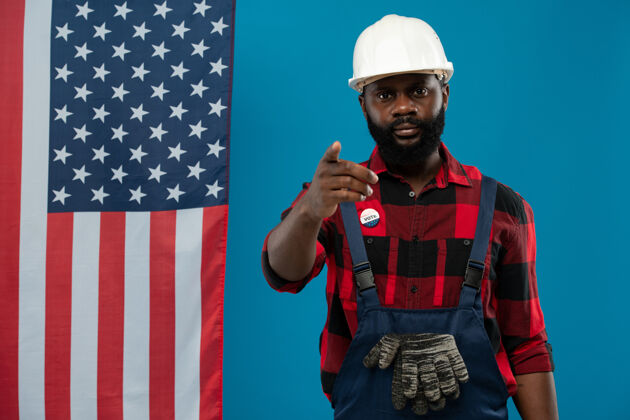 投票年轻的非洲建设者戴着安全帽 穿着工作服和法兰绒 站在镜头前指着你美国文化劳动美国国旗