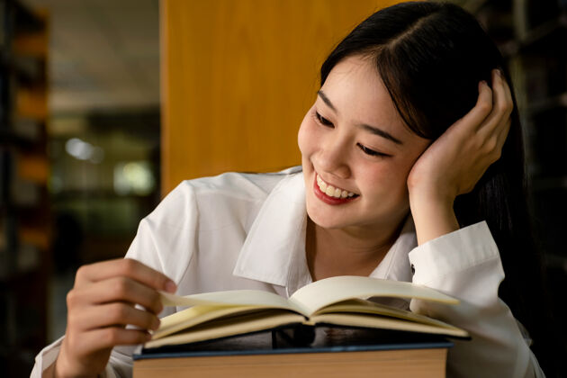 阅读年轻的亚洲女大学生在大学图书馆读书研究和向教科书学习学术站着大学