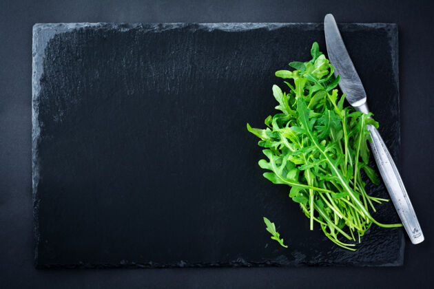 生的一堆新鲜的芝麻菜放在一块黑色的板岩黑板上意大利肉香菜叶