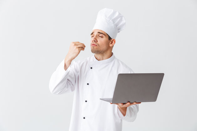 沟通开朗的厨师穿着制服站在白色的墙上 手里拿着笔记本电脑互联网笔记本电脑人