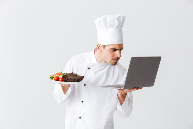 制服正经的厨师穿着制服站在白色的墙上 拿着笔记本电脑 展示着一道菜老板白种人人