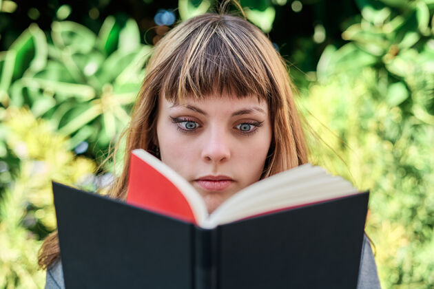教育一张蓝眼睛的白人金发年轻女子在公园看书的特写照女性金发女孩