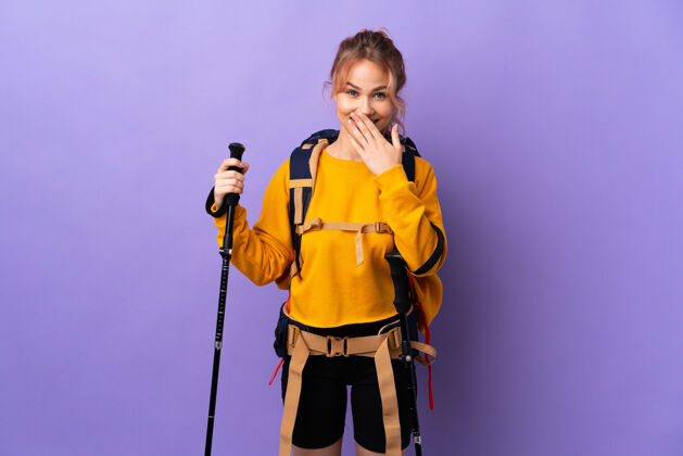 掩护背着背包和登山竿的女孩在孤独的紫色上快乐地笑着用手捏着圆锥形的嘴大笑人脸