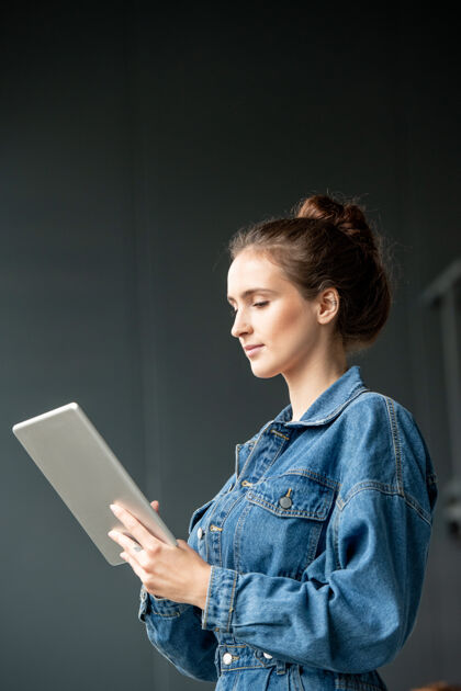 只有一个女人穿着牛仔休闲装的年轻黑发女上班族一边使用数码平板电脑一边浏览在线视频或信息触摸屏欢呼成功