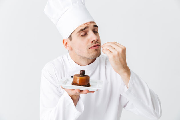 面包房开朗的厨师穿着制服 在白色的墙上展示一个盘子上的糕点厨房美味食物