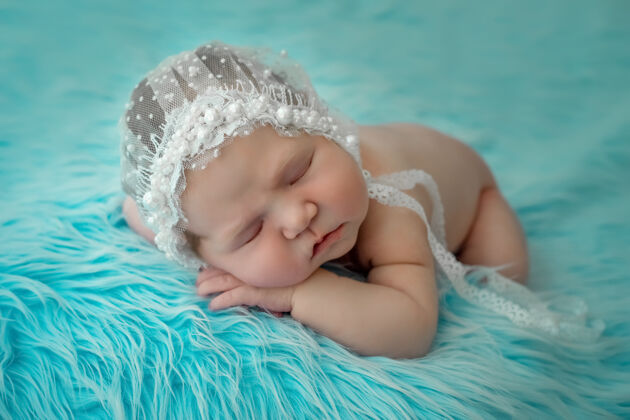 美丽一个刚出生的婴儿睡在蓝色背景的肚子上 双手交叉放在脸颊下面女孩宝贝新生儿
