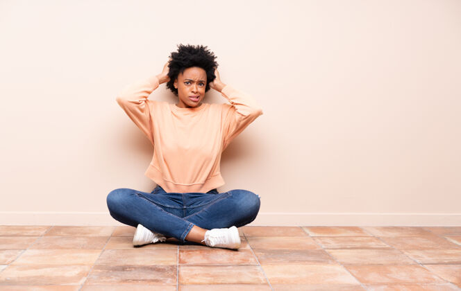 成人坐在地板上的非洲裔美国妇女沮丧地把手放在头上年轻房间身体