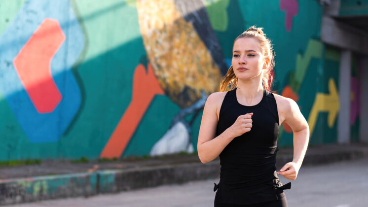 成人身着运动服的金发女郎在户外训练的路上奔跑 背景是五彩缤纷的墙壁运动装身体焦点