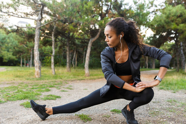 精力充沛20多岁的黑人黑人妇女身穿黑色运动服 在绿色公园里锻炼身体 伸展双腿跑步年轻非洲