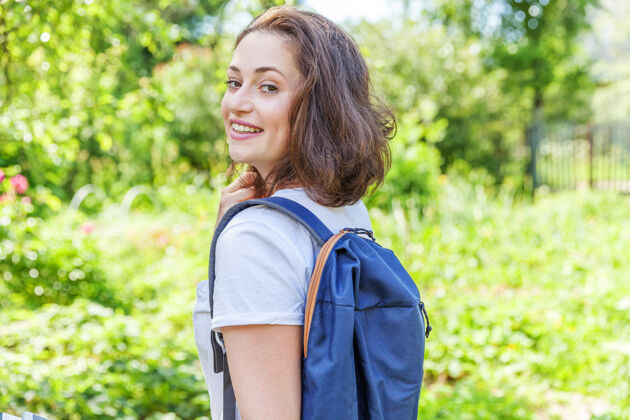 女孩快乐积极的女学生 背着背包 在绿色公园的背景下微笑着复制空间回来背景