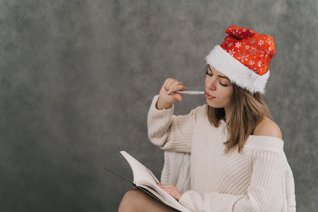 季节这个女孩为新来的女孩列了一张心愿单年份列表给…的礼物朋友女孩戴着圣诞帽写在笔记本上日记五颜六色写作